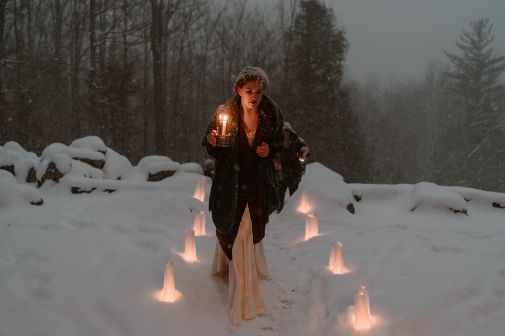 Bride walks a candelit aisle during an evening winter wedding in Lake Placid.
